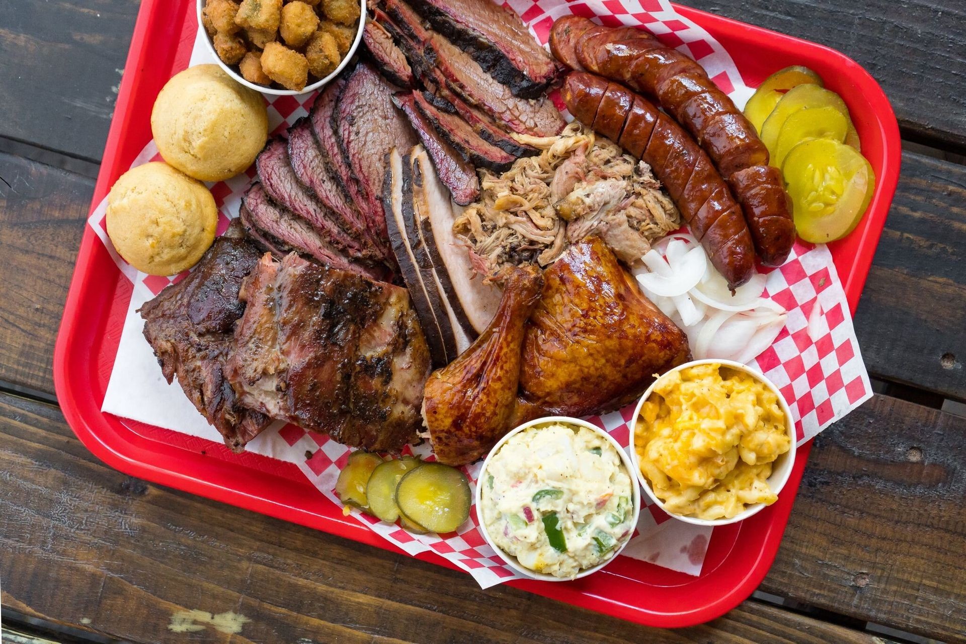 Tray filled with assorted barbecue meats, sides, and condiments on a checkered paper.