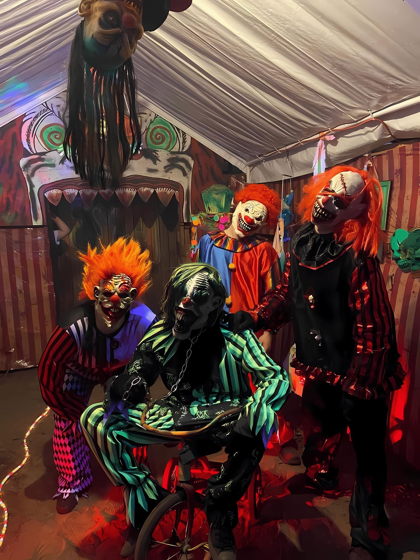 Group of people in various creepy clown costumes inside a Halloween-themed room with eerie decorations and lighting.